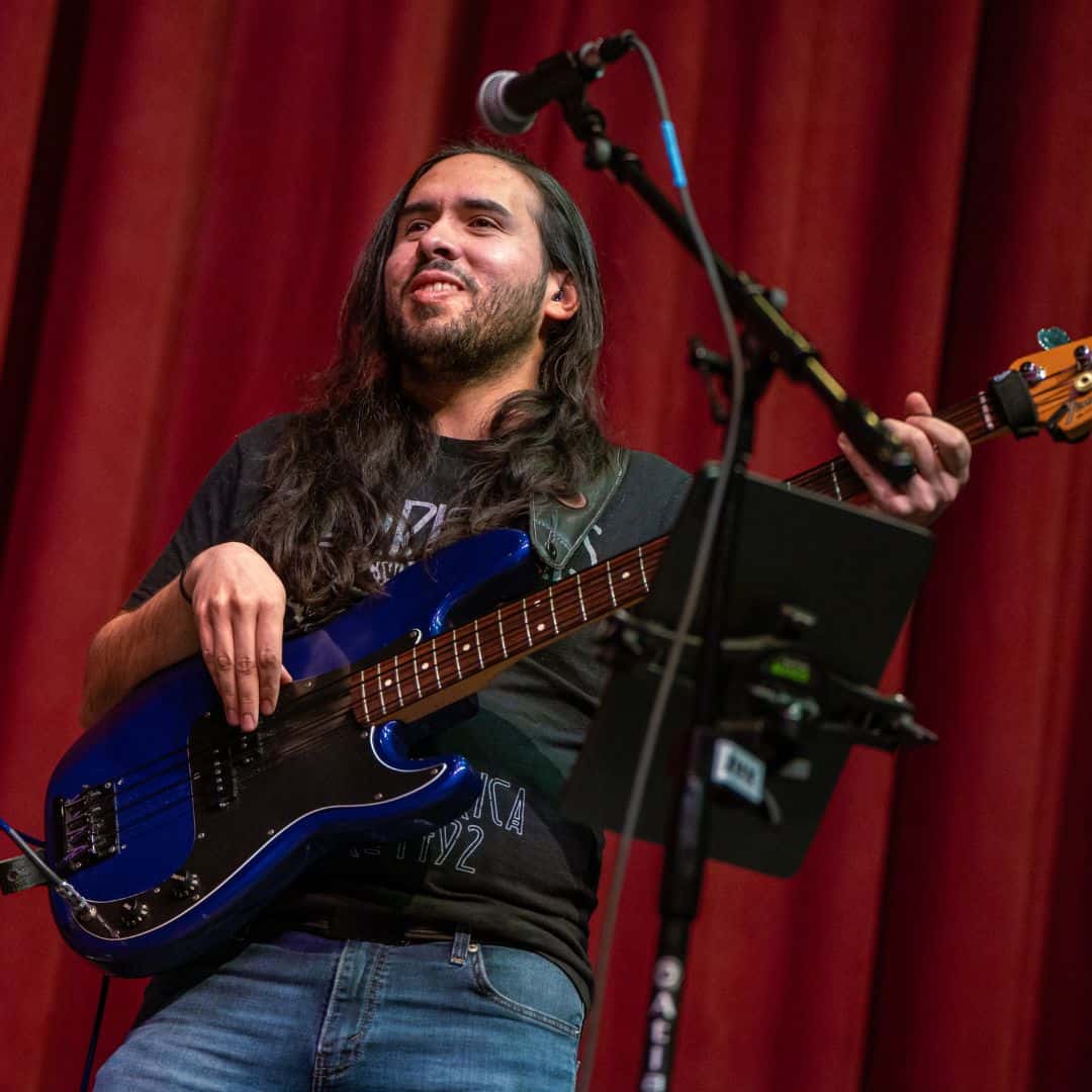 A photo of Josiah Contreras, a bass instructor at Swallow Hill Music in Denver, smiling while playing an electric bass.