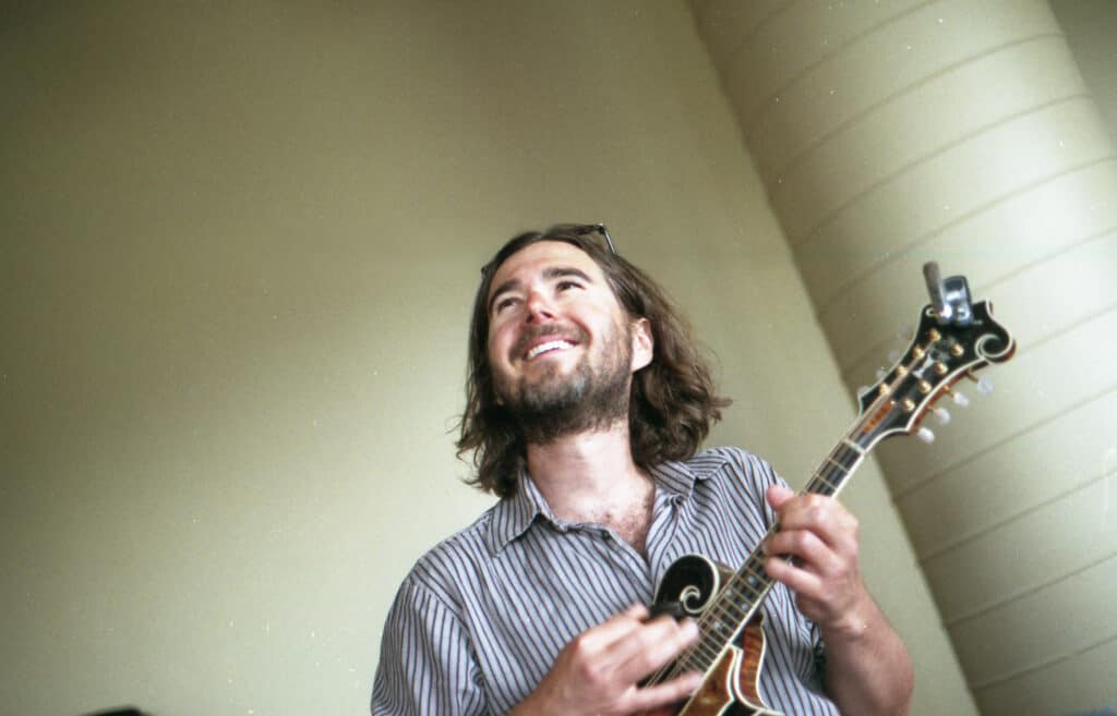 A young male student looks up and smiles while playing a mandolin.