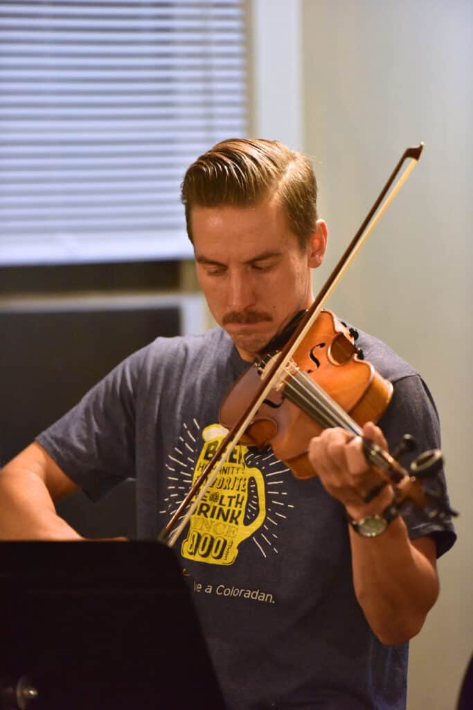 A man with a mustache looks with a focused expression down at sheet music while playing the violin during a fiddle class at Swallow Hill Music in Denver.