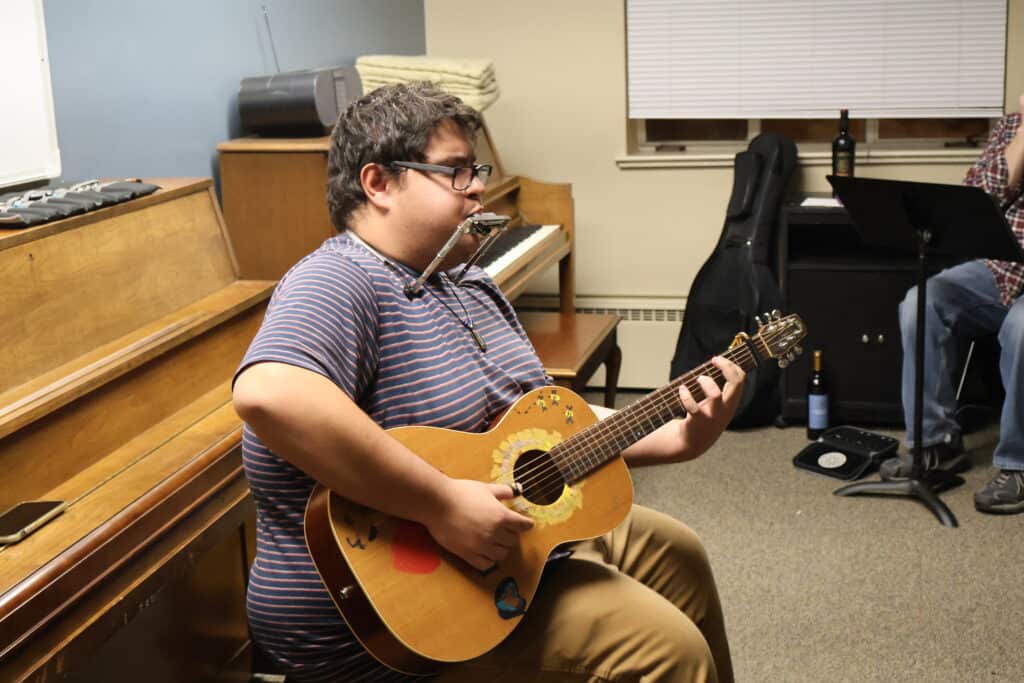 Swallow Hill Music instructor Nic Clark plays harmonica in a holder while also playing guitar during a harmonica group class.