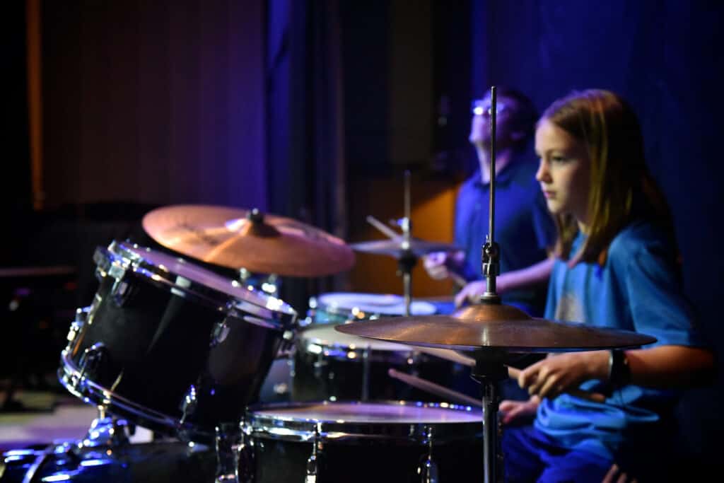 A young female student plays drum set on stage with an instructor during a percussion class at Swallow Hill Music in Denver.
