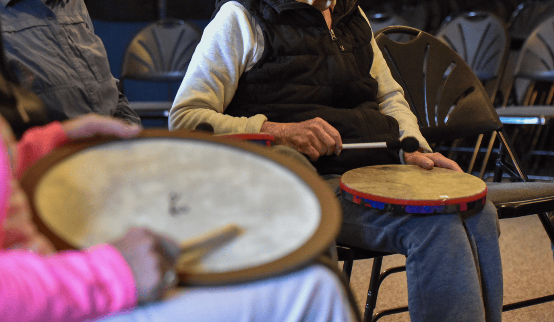 A photo of two older adults playing small drums with mallets in a music therapy session