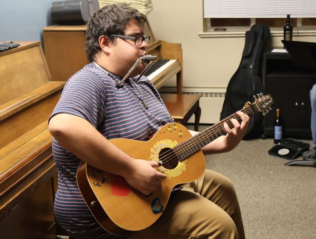 A man playing guitar while playing harmonica with a metal holder