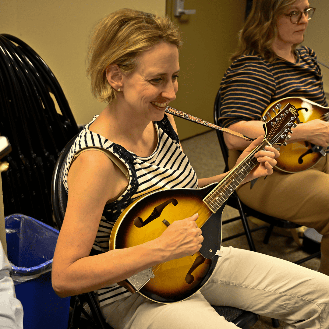 Two adult women look down at music stands while playing mandolins in a music class