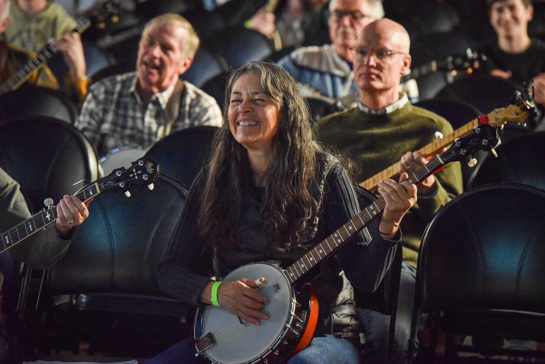 Woman smiling with banjo at Swallow Hill BanjoFest A photo of a woman smiling while playing the banjo seated with several other people sitting with banjos visible behind her during a workshop at Swallow Hill BanjoFest