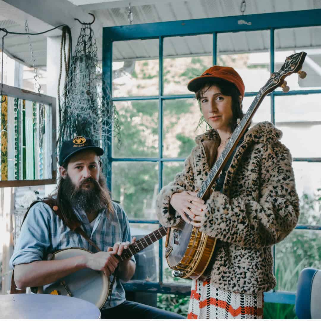 The Lowest Pair at Swallow Hill BanjoFest 2025 The two members of The Lowest Pair, Kendl Winter and Palmer T. Lee, posing for the camera with their banjos in a home