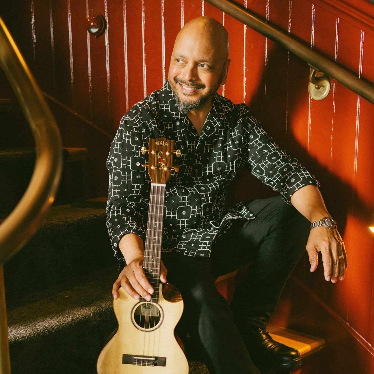 Denver UkeFest performer Steven Espaniola sits on a staircase smiling and holding his ukulele
